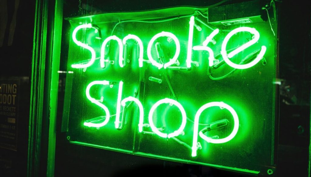 Green neon sign that writes "Smoke Shop"