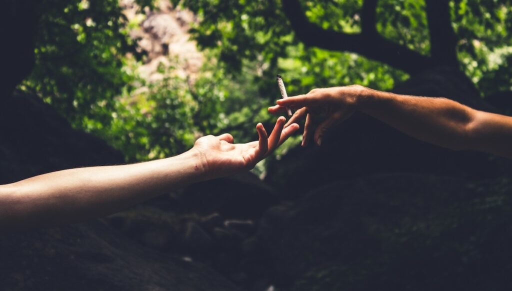 one hand holding a joint giving the joint to another hand